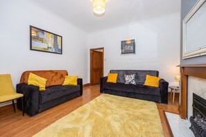 A living room with two sofas, a yellow armchair, a fireplace, and a rug.