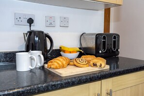A kitchen counter with a coffee maker, toaster, and a bowl of fruit and pastries.