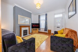 Een woonkamer met een open haard, een televisie en twee banken.