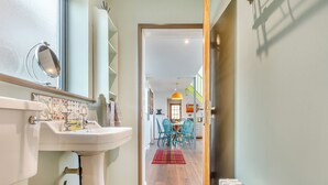 A bathroom with a sink, mirror, and towel rack. A hallway leads to a dining area with chairs and a table.