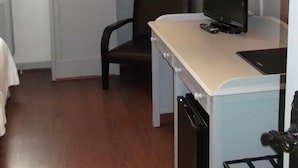 A compact room with a bed, a desk with a computer, a chair, a small kitchenette, and a window. - Hotel Comillas (Comillas)
