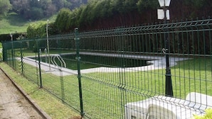 A fenced garden area with a pond, a lamp post, and a pathway. - Hotel Comillas (Comillas)