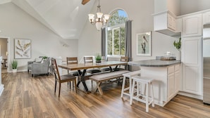 A spacious kitchen with a wooden dining table, white cabinetry, and a large island. - Sunset Retreat Sleeps 30 | Hot Tub | Ping Pong | (Stevensville)