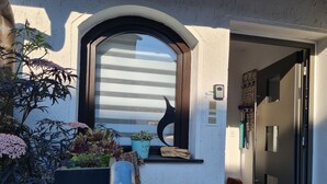 Ein moderner Eingangsbereich mit Glastür, einem kleinen Fenster mit Pflanzen und einer Überwachungskamera.