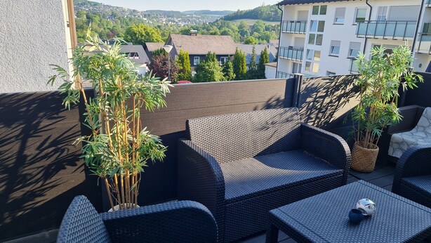 Eine Terrasse mit Korbmöbeln, darunter Sofas und ein Tisch, sowie zwei Kübelpflanzen.