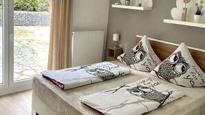 Ein Schlafzimmer mit einem großen Bett, einem Fenster mit Vorhängen, einem Heizkörper und Regalen an der Wand mit Dekorationen.