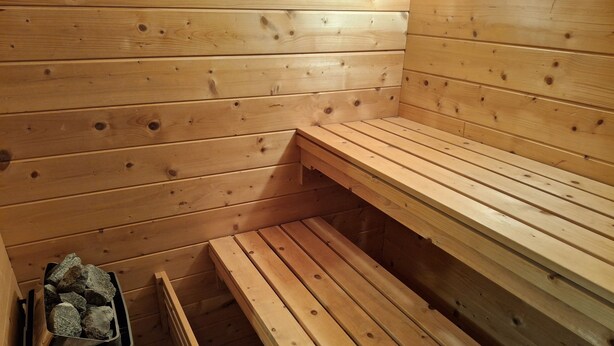 Sauna, jossa on puiset lauteet ja kivillä täytetty astia.