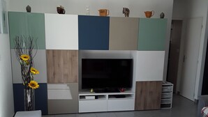 Ein modernes Wohnzimmer mit einem Flachbildfernseher, einem weißen Couchtisch, einem grauen Sofa und einer kleinen weißen Kommode.