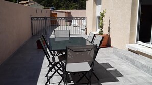 Eine Terrasse im Freien mit Tisch und Stühlen, einem Blumentopf und Blick auf eine Hügellandschaft.