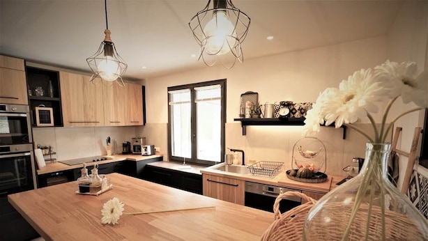 Une cuisine moderne avec des meubles en bois, un îlot central, des luminaires suspendus et des objets décoratifs.