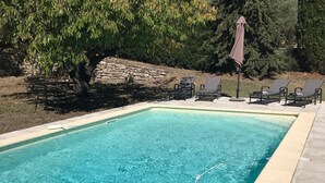 Une piscine rectangulaire à l’eau d’un bleu cristallin, entourée d’un mur de pierre et bordée d’une rangée de chaises longues.