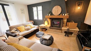 Un salon chaleureux avec une cheminée, des canapés à rayures et des poufs ronds.