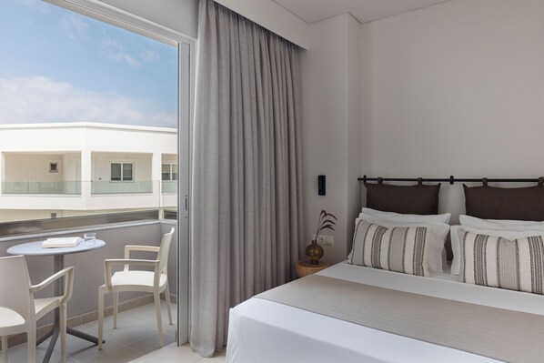 A hotel room with a bed, a small table with chairs, a window with curtains, and a view of a building outside. - Anastasia Hotel & Apts Kos (Kos)