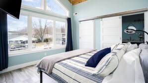 Un dormitorio con un ventanal grande, una cama con cubrecama a rayas y un ventilador de techo.