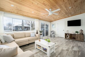 Ein modernes Wohnzimmer mit Holzboden, einem weißen Sofa, einem Couchtisch und einem Fernseher an der Wand.