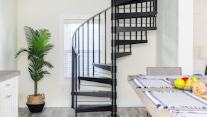 Una cocina moderna con una escalera espiral negra, una planta en maceta y un comedor con una mesa lista para dos.