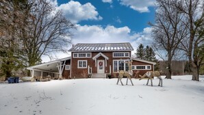 Ein zweistöckiges Haus mit verdeckter Veranda, einer Haustür mit Adventskranz und einem schneebedeckten Garten.