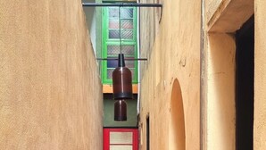 Un estrecho callejón con una puerta roja al final, un colgante de luz y un ventanal verde.
