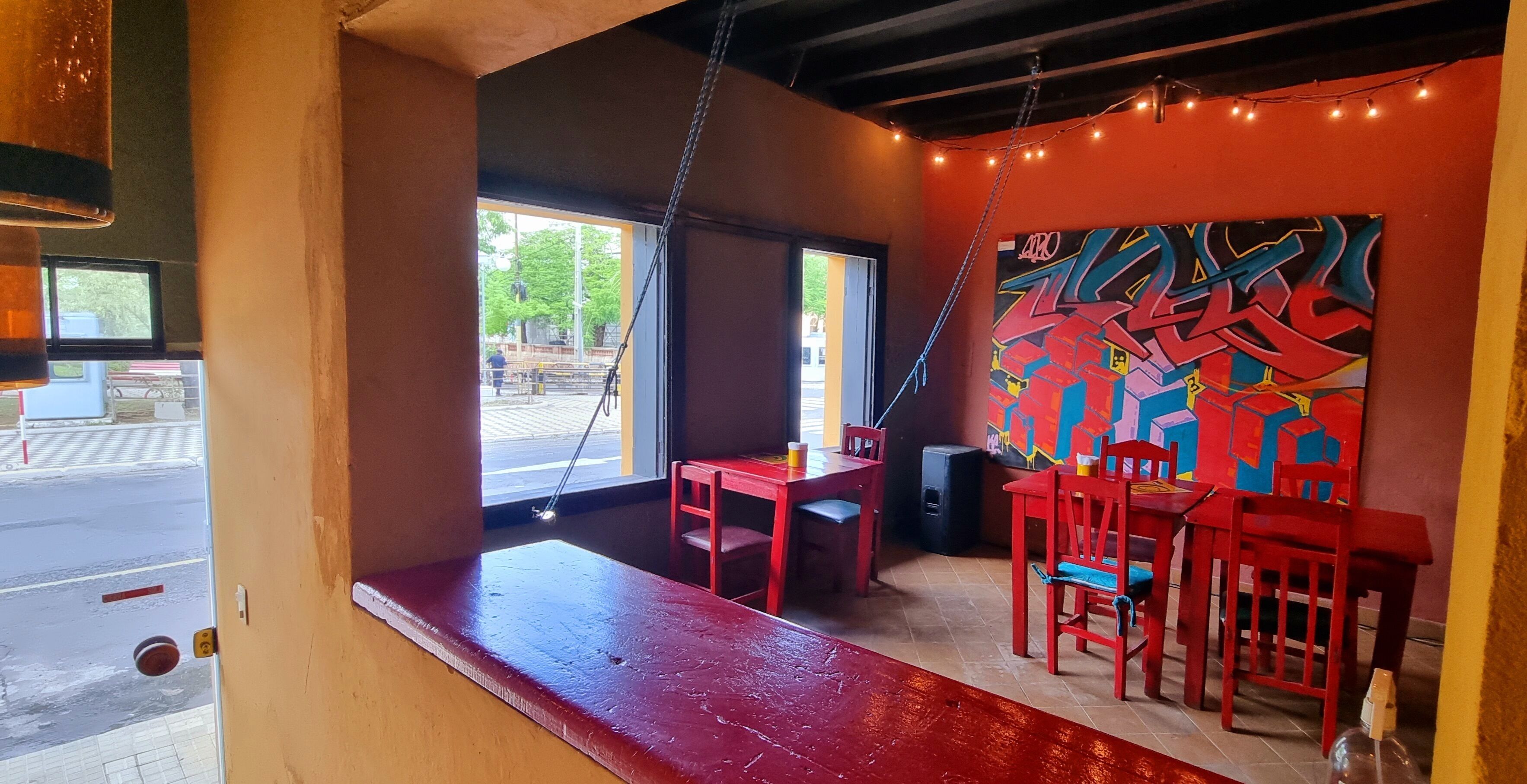 Un interior con un banco rojo, sillas rojas, una pared con grafitis coloridos y una ventana que da a la calle.