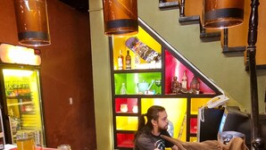 Una zona de bar con mostrador, luces colgantes y una escalera al fondo.