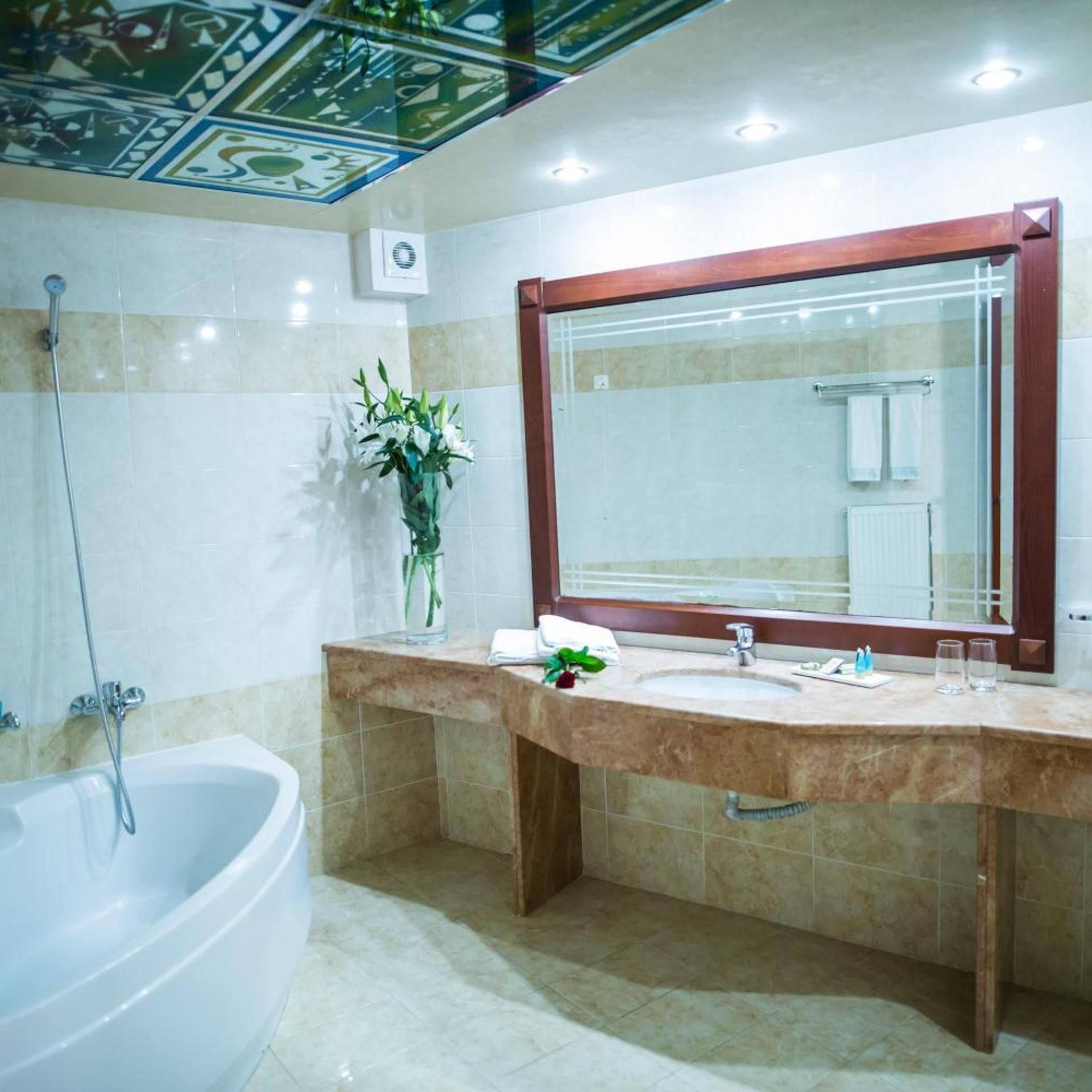 A bathroom with a bathtub, a large mirror, and a sink with a vase of flowers.