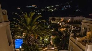 Vista nocturna de un hotel con varios pisos, iluminación exterior y una zona de piscina rodeada de vegetación.