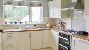 Una cucina con mobili bianchi, un lavello, un piano cottura e una finestra con vista sul verde.