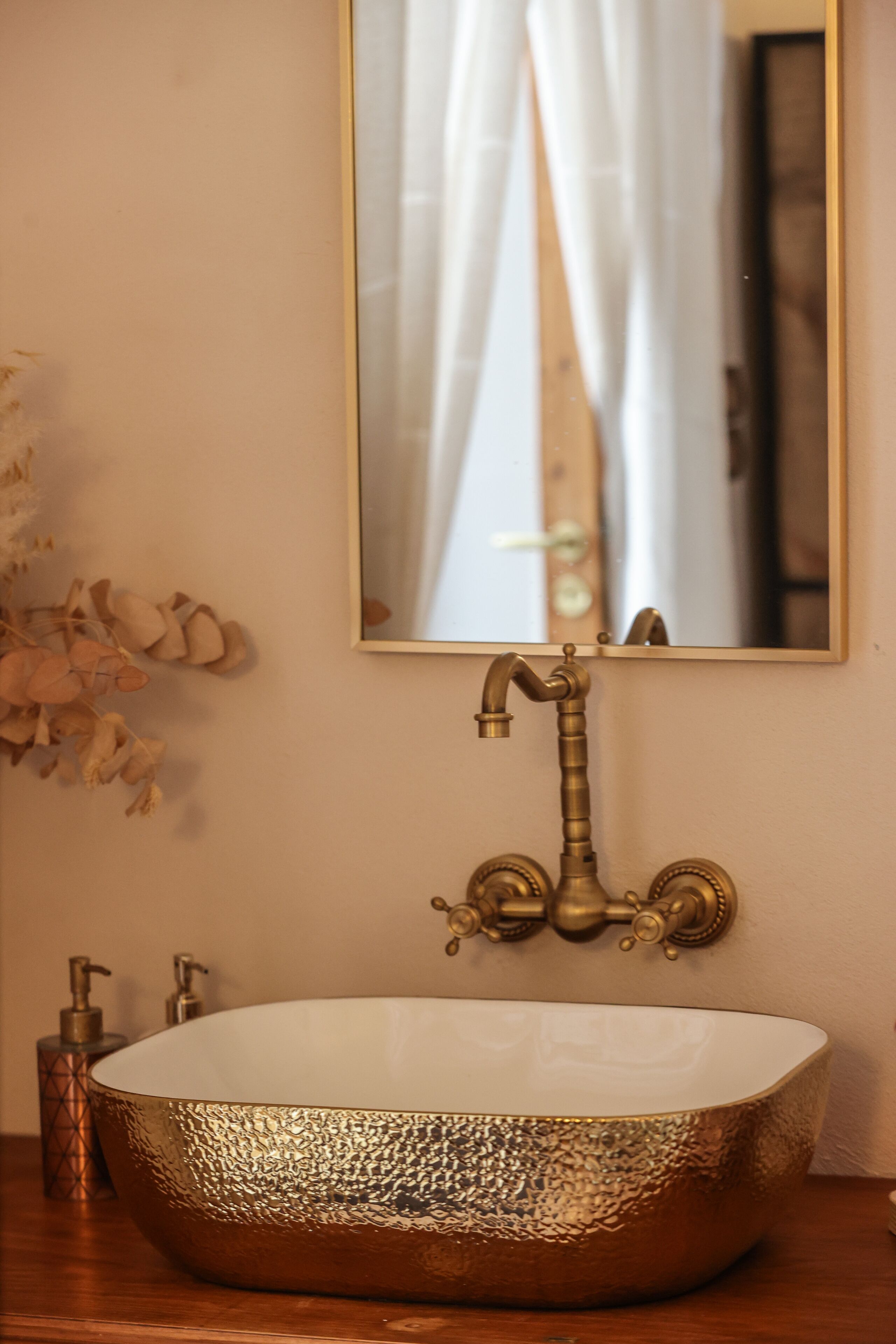 A bathroom with a gold-colored vessel sink, a mirror, and a wooden vanity.