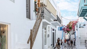A narrow street with white buildings, stone paving, and a wooden staircase. - Sikate Hospitality (Mykonos)