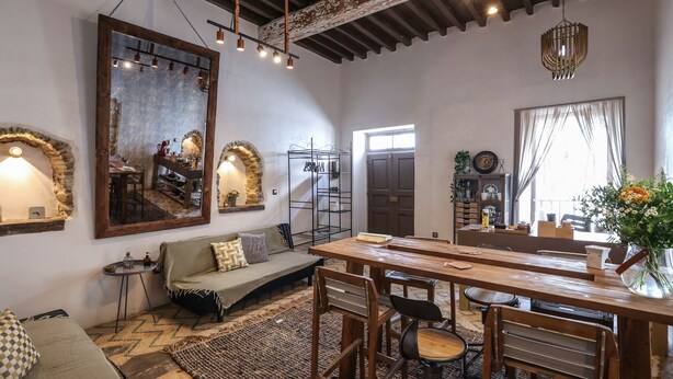 A cozy living area with a sofa, a dining table with chairs, a large mirror, and a rustic ceiling. - Sikate Hospitality (Mykonos)