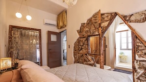 A bedroom with a large bed, a chandelier, and a stone wall. - Sikate Hospitality (Mykonos)