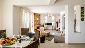 A modern living room with a fireplace, a dining area with fruit, and a sofa. - Cape Greco Villa Anastel 2 (Ayia Napa)