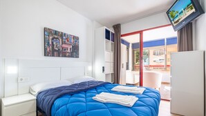 A hotel room with a bed, a television, a painting, and a view of the outside.