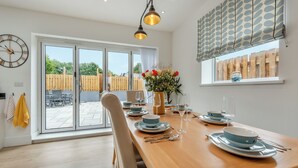 A dining area with a wooden table set for four, a large window with a view of the outdoors, and a clock on the wall. - 3 bedroom accommodation in Square and Compass, near Haverfordwest (Square and Compass, near Haverfordwest)