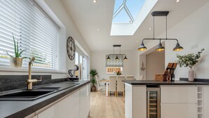 A modern kitchen with a central island, a dining area with chairs, a clock, and a skylight. - 3 bedroom accommodation in Square and Compass, near Haverfordwest (Square and Compass, near Haverfordwest)