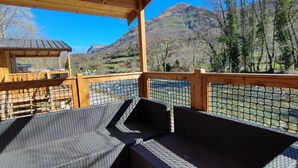 Um deck de madeira com móveis de vime, com vista para um rio e montanhas.
