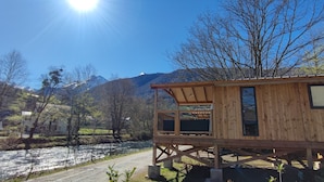 Uma cabana de madeira com varanda, vista para um rio e montanhas.