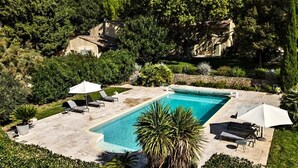 A rectangular swimming pool with lounge chairs and umbrellas, surrounded by greenery and stone walls. - 18th century Provencal country house (Sarrians)