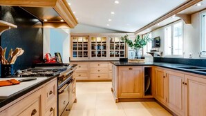 A modern kitchen with wooden cabinets, a black stove, and a large window. - 18th century Provencal country house (Sarrians)