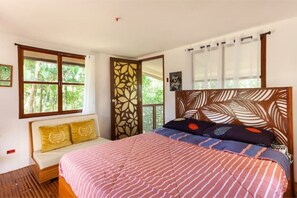 Relax in a serene space with a large bed, wooden headboard, and a view of lush greenery.