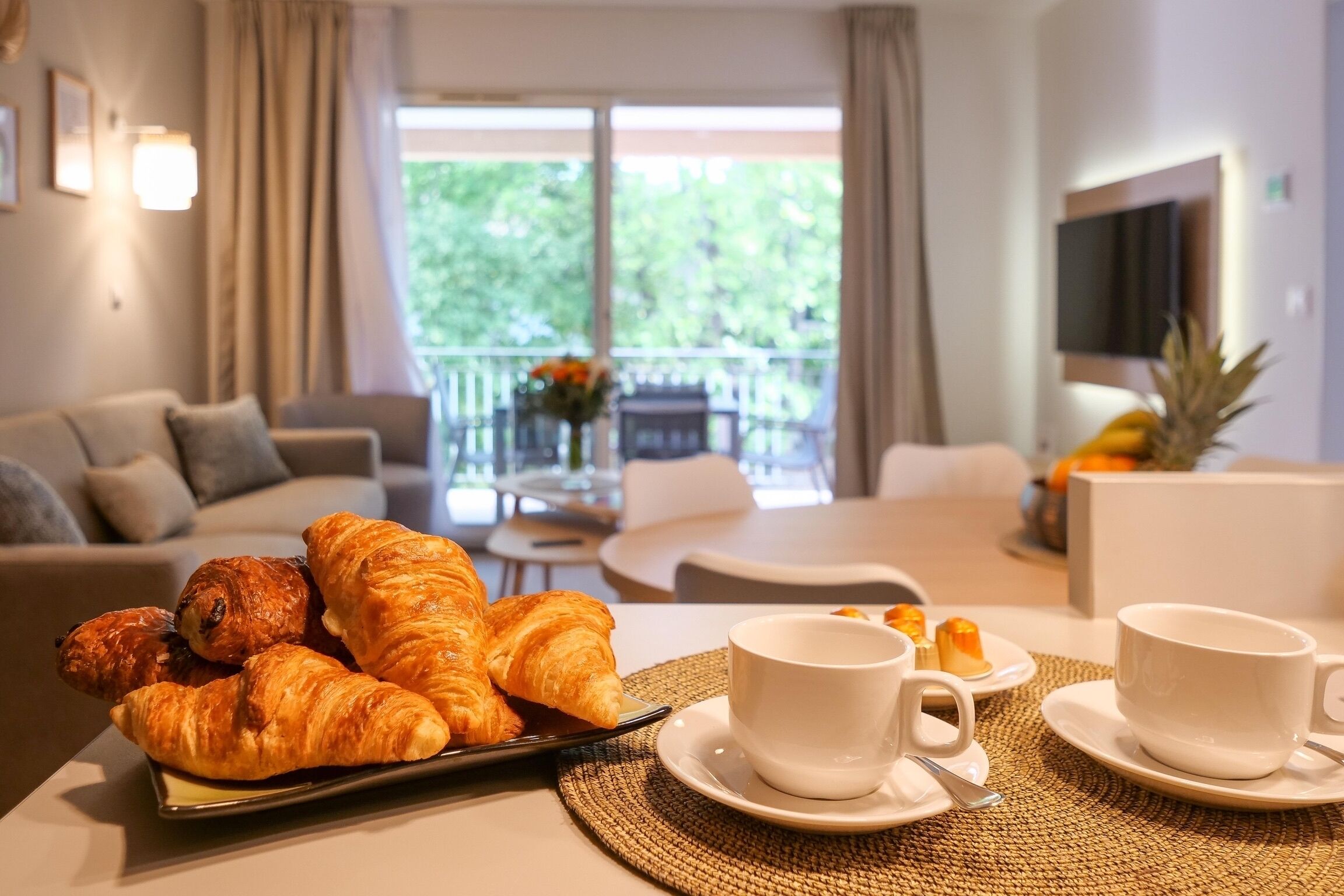 A dining area with croissants, coffee cups, and a pineapple on a table.