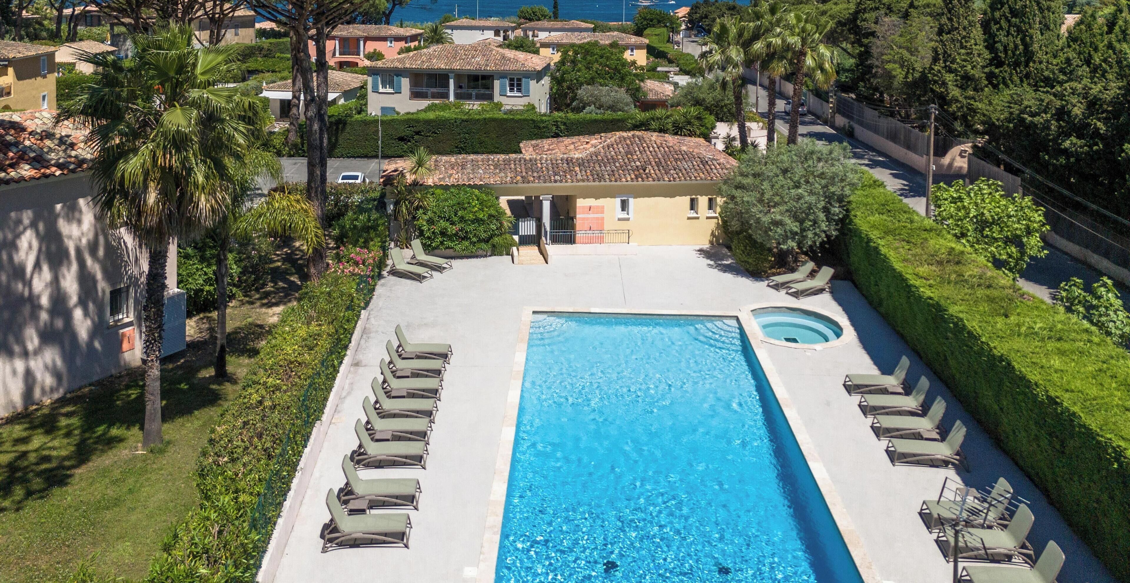 A rectangular swimming pool with a hot tub, surrounded by lounge chairs, and a view of residential buildings.