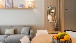 Ein modernes Wohnzimmer mit einem grauen Sofa, einem Holzesstisch mit Obstschale und einem Spiegel an der Wand.