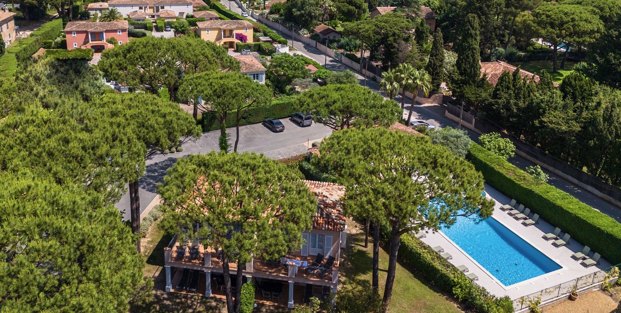 An aerial view of a residential area with a swimming pool, a covered outdoor seating area, and surrounding greenery.