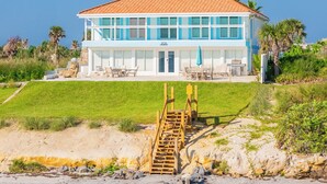 Une maison à deux étages, avec un toit recouvert de tuiles, un patio abrité avec des meubles d’extérieur et un escalier menant à l’entrée.