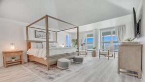 Une chambre à coucher avec un lit à baldaquin, une table de chevet en bois, une petite table d’appoint, une grande fenêtre avec des rideaux et une vue sur l’extérieur.
