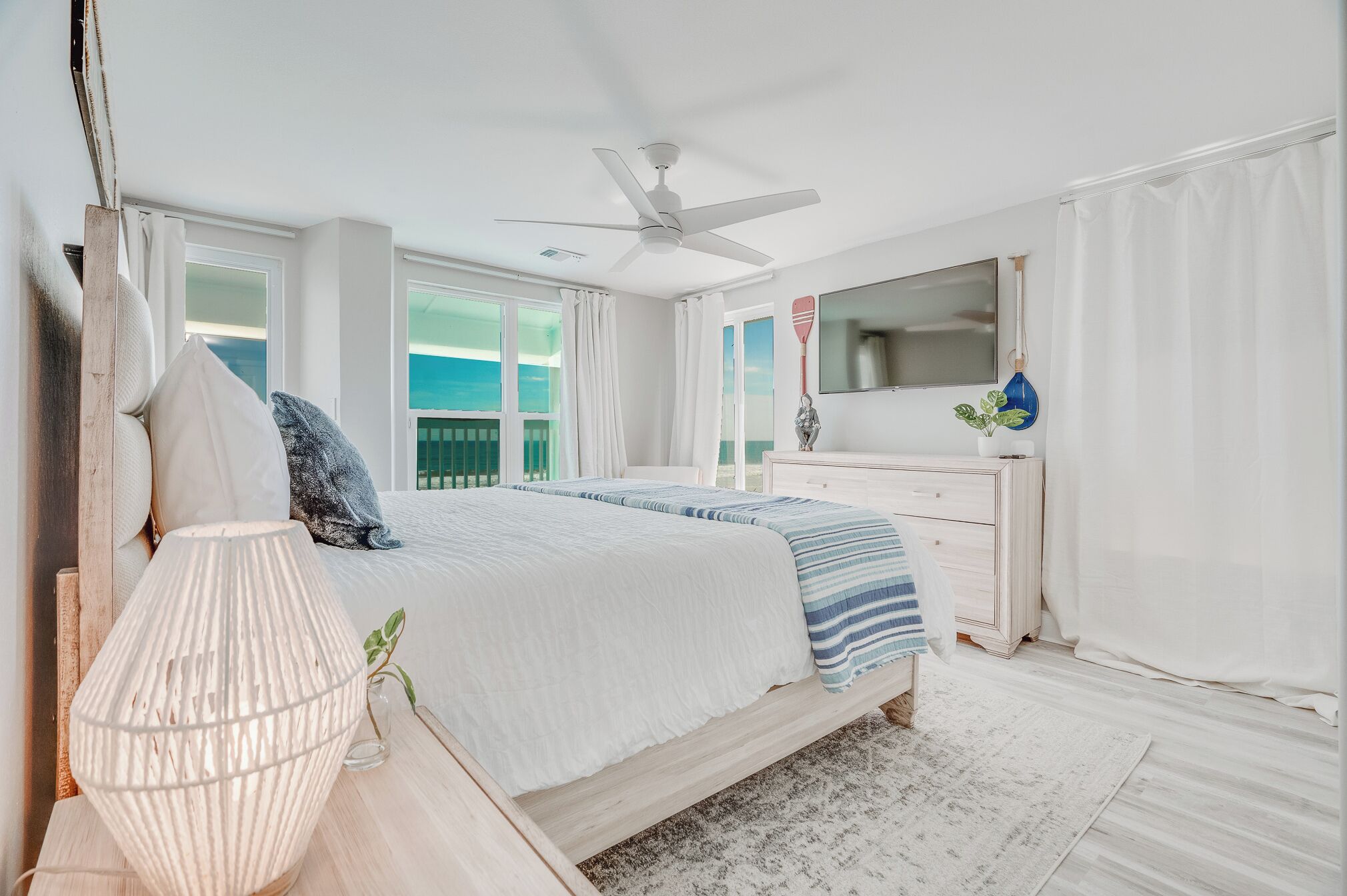 A bedroom with a bed, a nightstand, a lamp, a dresser, a mirror, and a ceiling fan.
