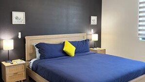 A bedroom with a bed, wooden headboard, two bedside tables with lamps, a ceiling fan, and two framed pictures on the wall. - OranGe DeLuxe - No Cleaning Fee, Centrally Located. (Omaha)