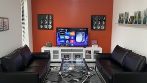 A living room with two black leather sofas, a glass coffee table, a flat-screen TV, and a ceiling fan. - OranGe DeLuxe - No Cleaning Fee, Centrally Located. (Omaha)