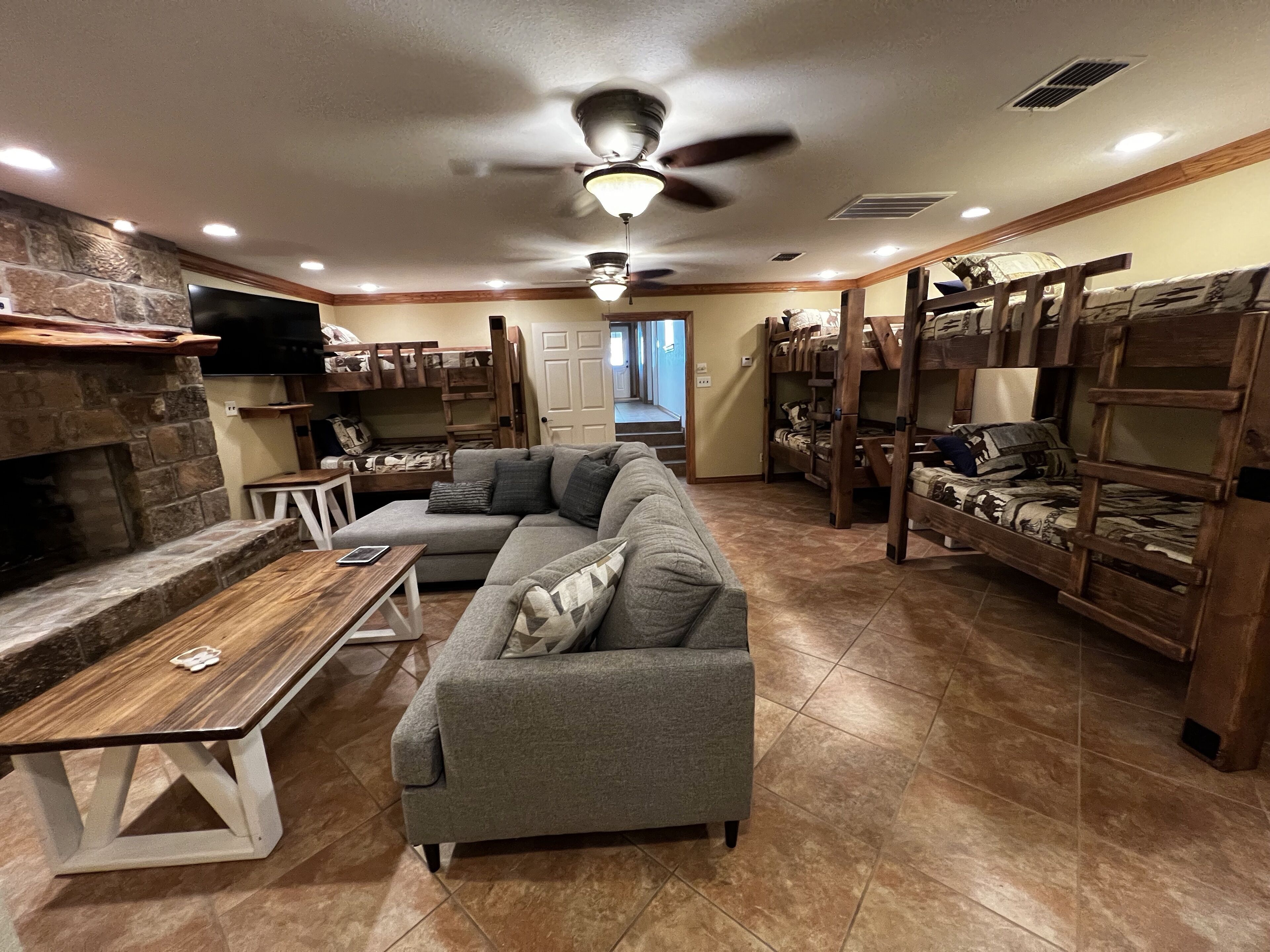 A cozy living room with a stone fireplace, a gray sectional sofa, and wooden bunk beds.